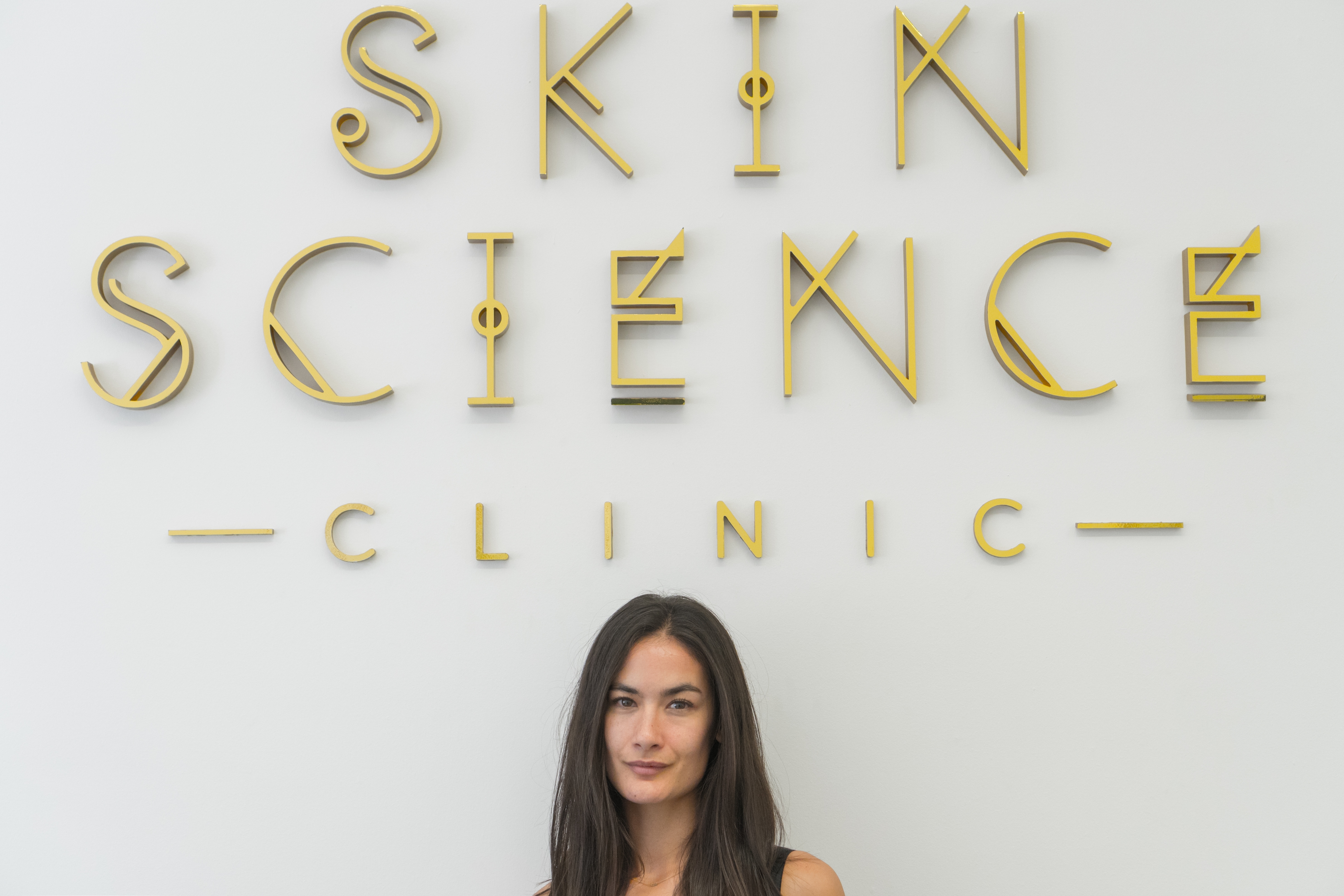 A patient beneath the gold Skin Science Clinic signage in the clinic reception